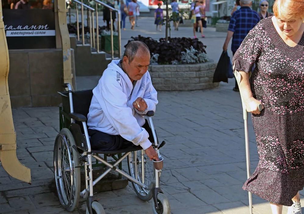 На фото инвалид без ног на инвалидной коляске на улице города собирает деньги и прости милостыню, по сути занимается попрошайничеством.