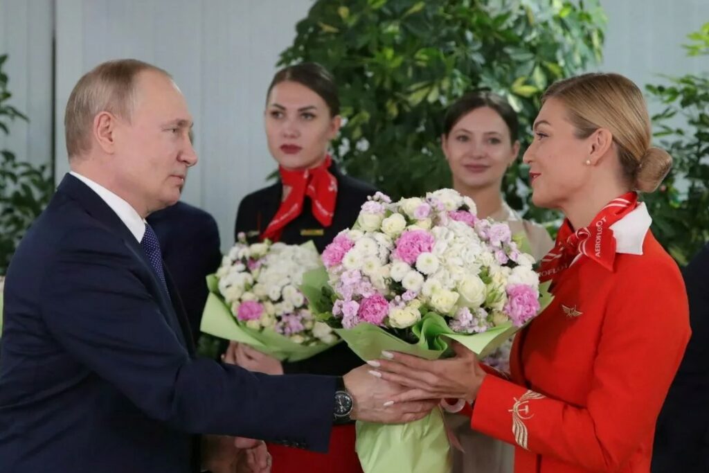На фото Путин дарит цветы женщинам.