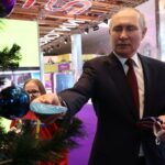 На фото Путин снимает с новогодней елки подарок для ребенка.