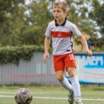 На фото мальчик играет в футбол в спортивной форме команды Спартак.